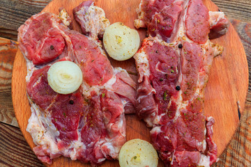 Fresh raw pork meat with spices and onion on wooden cutting board on rustic table. Top view