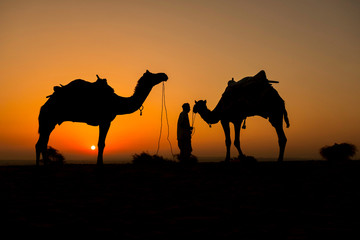 Silhouette of camel trader crossing the Thar Desert in Jaisalmer, India.