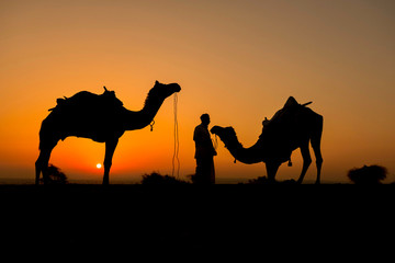 Silhouette of camel trader crossing the Thar Desert in Jaisalmer, India.