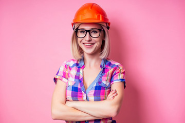 Female painter using roller for refurbishing color of pink wall indoors.smiling woman in business checkered shirt wearing builder helmet painting the walls in the apartment