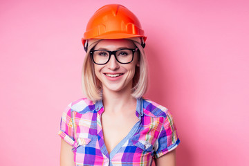 Female painter using roller for refurbishing color of pink wall indoors.smiling woman in business checkered shirt wearing builder helmet painting the walls in the apartment