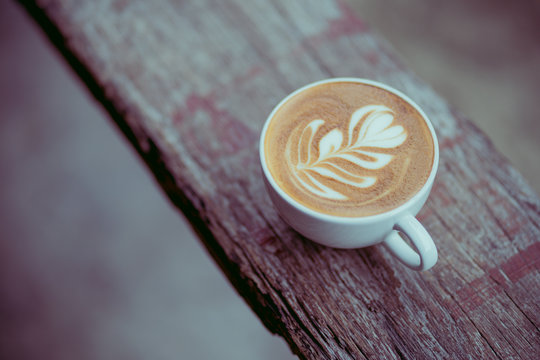 a cup of hot latte coffee on aged brown wood, heart shape latte art, coffee lover concept, vintage tone
