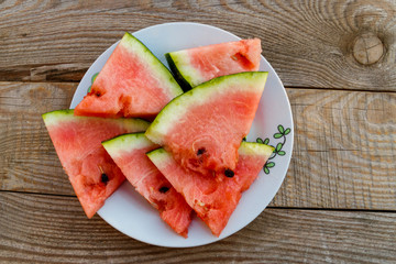 Fresh ripe sliced watermelon in white plate on rustic wooden table