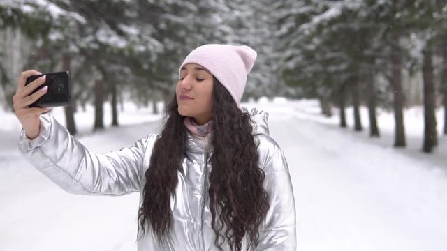 A girl makes selfie using a smartphone in the winter forest