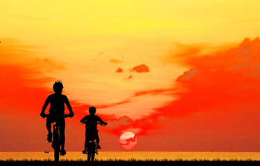 Fototapeta na wymiar silhouette Father and son riding bicycle at sunset sky