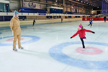 Full length portrait of happy little girl figure skating in indoor rink with  coach giving...