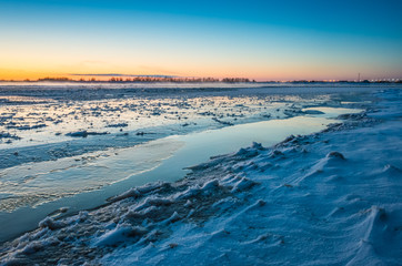 Naklejka na ściany i meble Winter landscape with sunset. Most of the frame takes a snowy field.