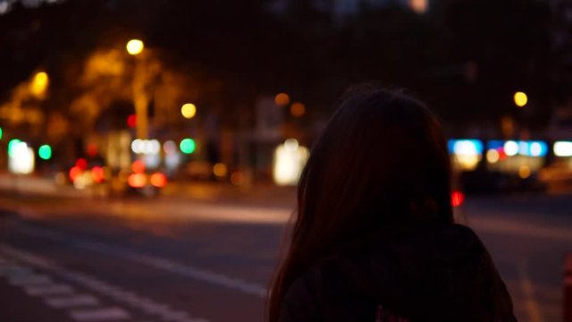 Young woman crossing the traffic road at night in the city centre alone.