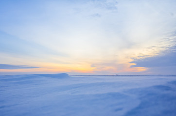 Winter landscape with sunset. Most of the frame takes a snowy field.