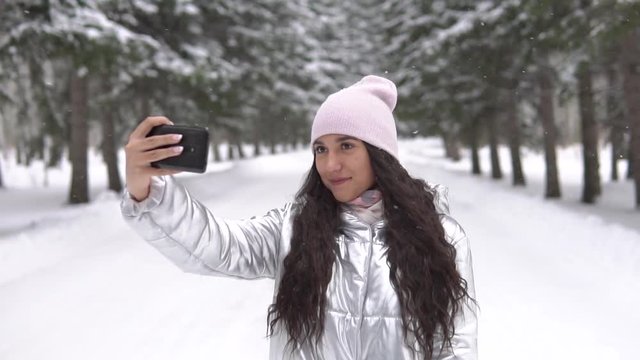 Girl makes selfie using smartphone while standing in a winter forest