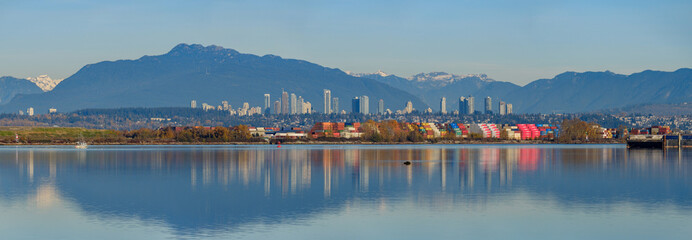 Panoramic view of cargoes at dock with colourful reflection on the river and city skyline and mountains at background at Richmond, BC - 234217896