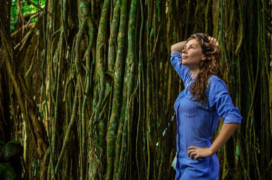 portrait of nice young woman is taking picture in the jungle with lians. The girl stands by the tree beside her. The loneliness of a girl who is alone in the jungle