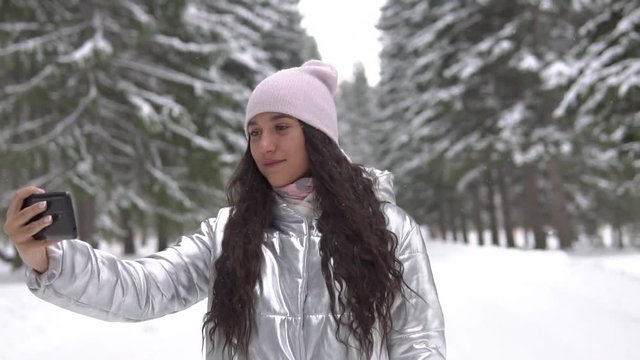 Young girl makes selfie using smartphone while standing in the winter forest
