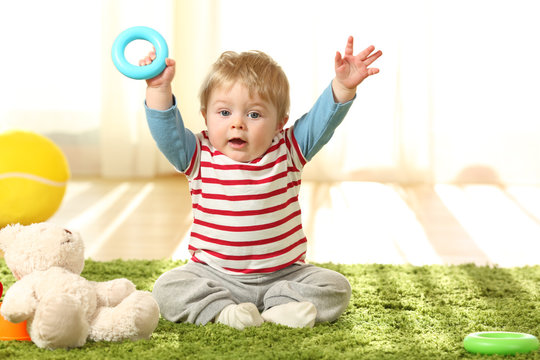 Happy Baby Raising Arms With A Toy On The Floor