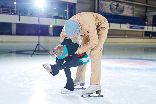 Full length portrait of female coach helping little girl doing figure skating moves in indoor rink, copy space
