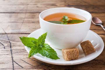 Cup of hot tea with mint and brown sugar on a wooden table