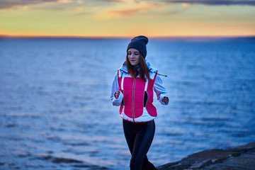A young girl in a sports hat and jacket makes a morning jog on the embankment in the morning before...