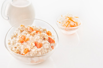 Oatmeal with pumpkin and nuts in a glass plate and a jug with milk on a white background. Close-up. Copy space