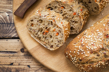 Fresh bread with sunflower seeds, sesame seeds and flax are cut into pieces on a cutting board.