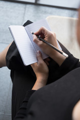 Beautiful woman with curly hair dressed on black wearing glasses and writing on a notebook with a black pencil