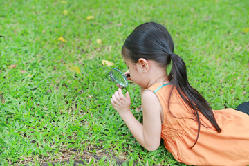 Little Asian child girl with magnifying glass on green grass garden. Close-up nature as researcher.