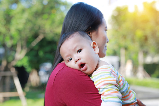 Portrait of Asian baby boy lying in hug of mother with looking camera.