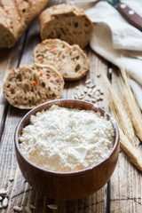Flour in a wooden bowl and pieces of grain bread on a wooden background