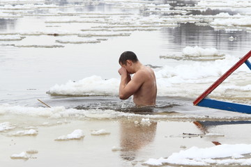 Man swims in cold water outdoor - Faith, Christianity, religion, baptism, winter bathing ritual in the ice hole on the river among the ice floes