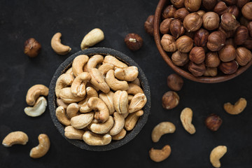 Mixed nuts on black concrete background, top view. Cashews and hazelnuts in bowl