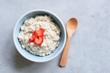Oatmeal porridge with strawberries on grey concrete background, top view with copy space for text