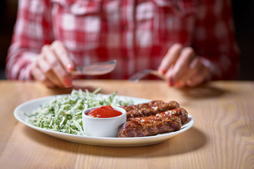 Woman cuts sausage grill with a fork and knife in a restaurant, in a red plaid shirt. selective focus.restaurant. copy space for design menu