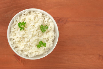 An overhead photo of a bowl of cooked white long grain rice, shot from the top on a dark rustic wooden background with a place for text