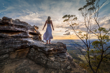 Standing on a cliff edge with dress blowing in the wind she dreams