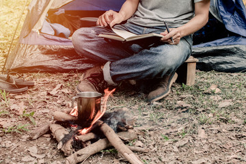 Asian young man sitting is reading a book in outside the tent. Alone camping in forest.