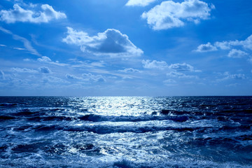 Fototapeta na wymiar sea and sunlit blue sky with clouds the sunlit is glistening white off a deep blue sea