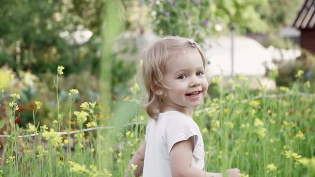 Little girl in yellow flowers in meadow on summer day looks at camera and smiles