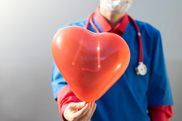 Doctor holds a red heart balloon in his hand. Healthcare patient care clinic concept.