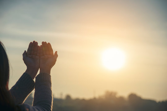 Asian woman praying and hopeful for peace the world.Christian women raise hands in hands together with sunrise background,believes and faith in christian religion.Prayer and hopeful concept.