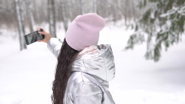 A girl makes selfie using a smartphone in the winter forest 4K