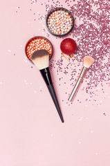 Fototapeta na wymiar Different Cosmetic makeup brushes, blush powder balls, christmas balls, holographic glitter confetti in the form of stars on pink background Flat lay top view copy space. Makeup accessories, holiday