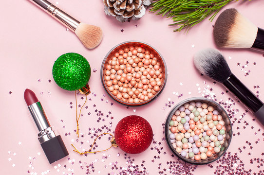 Cosmetic makeup brushes, blush powder, christmas balls, lipstick, holographic glitter confetti in the form of stars on pink background Flat lay top view copy space. Makeup accessories, holiday