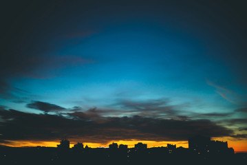 Cityscape with wonderful varicolored vivid dawn. Amazing dramatic blue cloudy sky above dark...