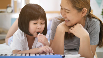 Happy little Asian girl playing melodica blow organ with mother