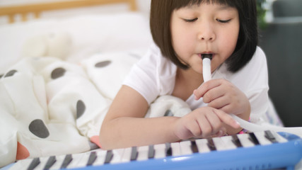 Happy little Asian girl playing melodica blow organ