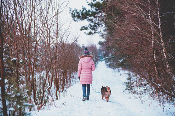 Fototapeta na wymiar Young woman with the dog walks in the snowy pine forest in winter