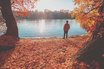 A man standing on the river bank in autumn and looking at water
