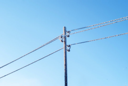 Icy Wires In The Frost On The Power Line Against The Blue Winter Sky..