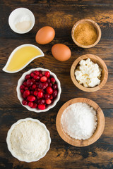 Ingredients for muffins. Flour, eggs, olive oil, cranberries, ricotta, brown and icing sugar, baking powder, vanilla. White bowls on wooden rustic table, top view
