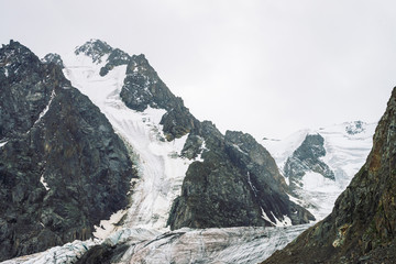 Snow on mountain range. Atmospheric snowy ridge under cloudy sky. Wonderful giant rocks in overcast weather. Climb high in mountains. Amazing minimalistic landscape of majestic nature of highlands.