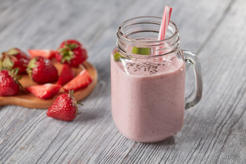 Healthy milk drink with strawberries, chia seeds and fresh mint leaves in a jar with a straw on a gray wooden background with copy space.